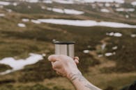 一只纹身的手拿着一个不锈钢杯子，在苏格兰白雪皑皑的风景中