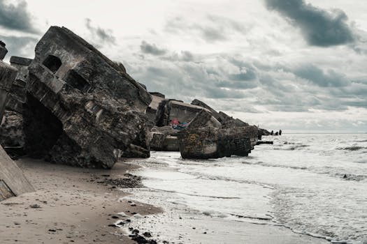 Concrete ruins on a sandy beach under a cloudy sky. Moody and dramatic scene.