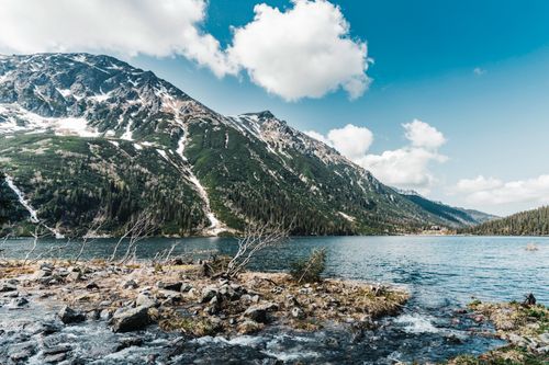 Free A serene mountain landscape showcasing a clear lake and snow-capped peaks under a bright blue sky. Stock Photo