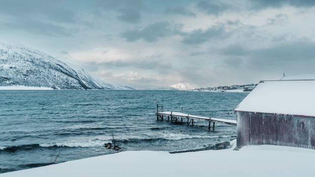 Snow-covered fjord landscape with a pier and mountains in Norway during winter.