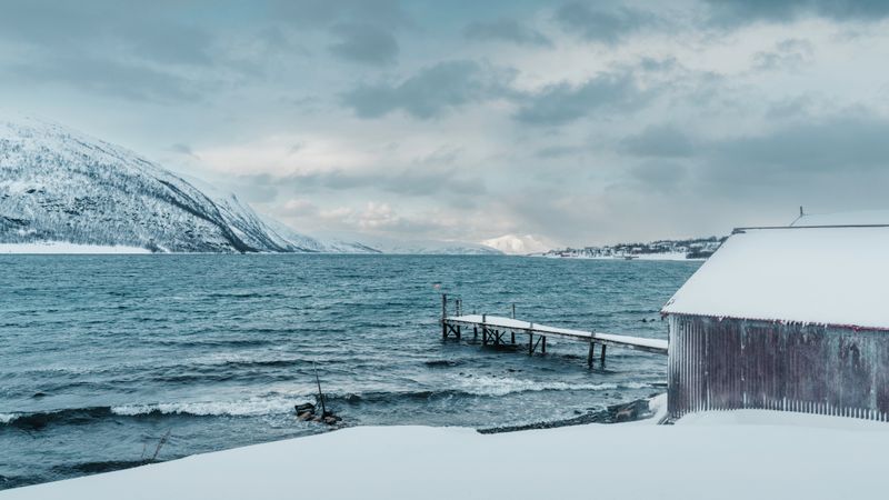 Fiord norvegian cu ponton și munți înzăpeziți pe timp de iarnă