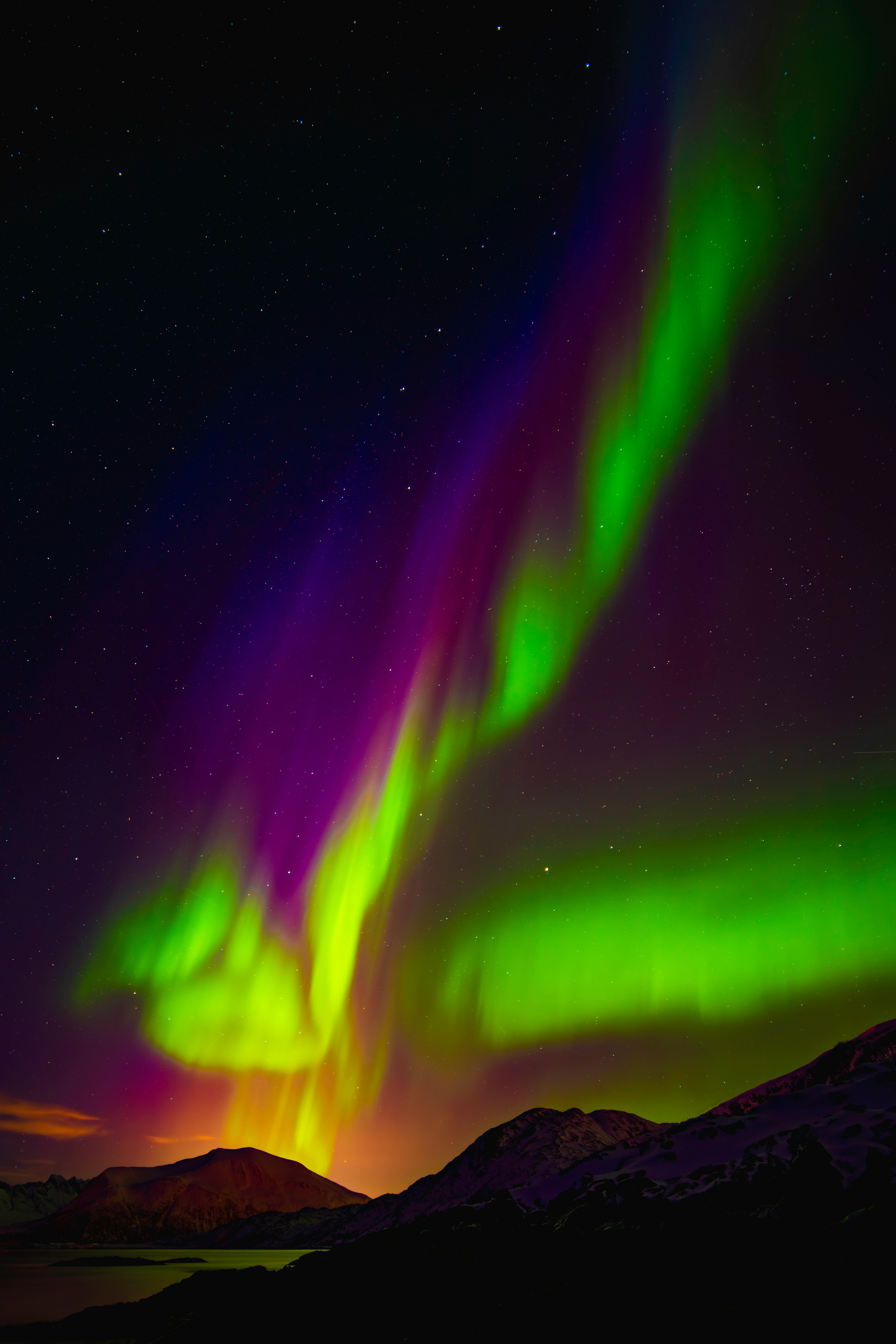 Stunning Northern Lights illuminate the sky over snow-capped mountains in Norway.