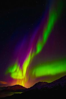 Stunning Northern Lights illuminate the sky over snow-capped mountains in Norway.