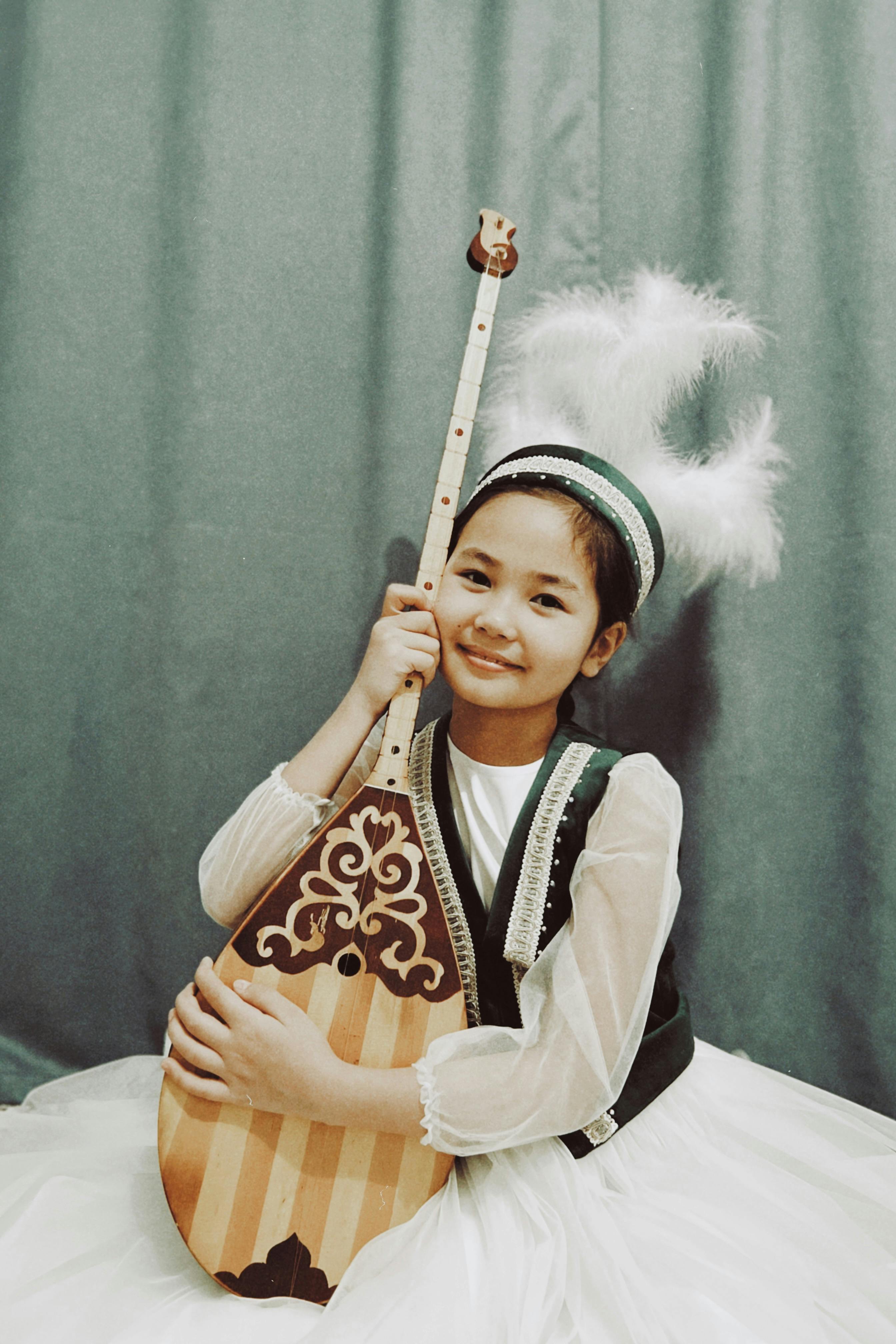 A smiling girl in traditional Kazakh clothing holding a dombra in Talgar, Almaty Region.