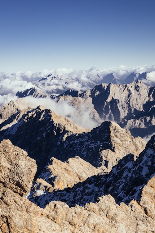 Vue Aérienne De La Chaîne De Montagnes De Roche Brune Et Grise Avec Des Formations Nuageuses Rampant Sur Ses Pentes
