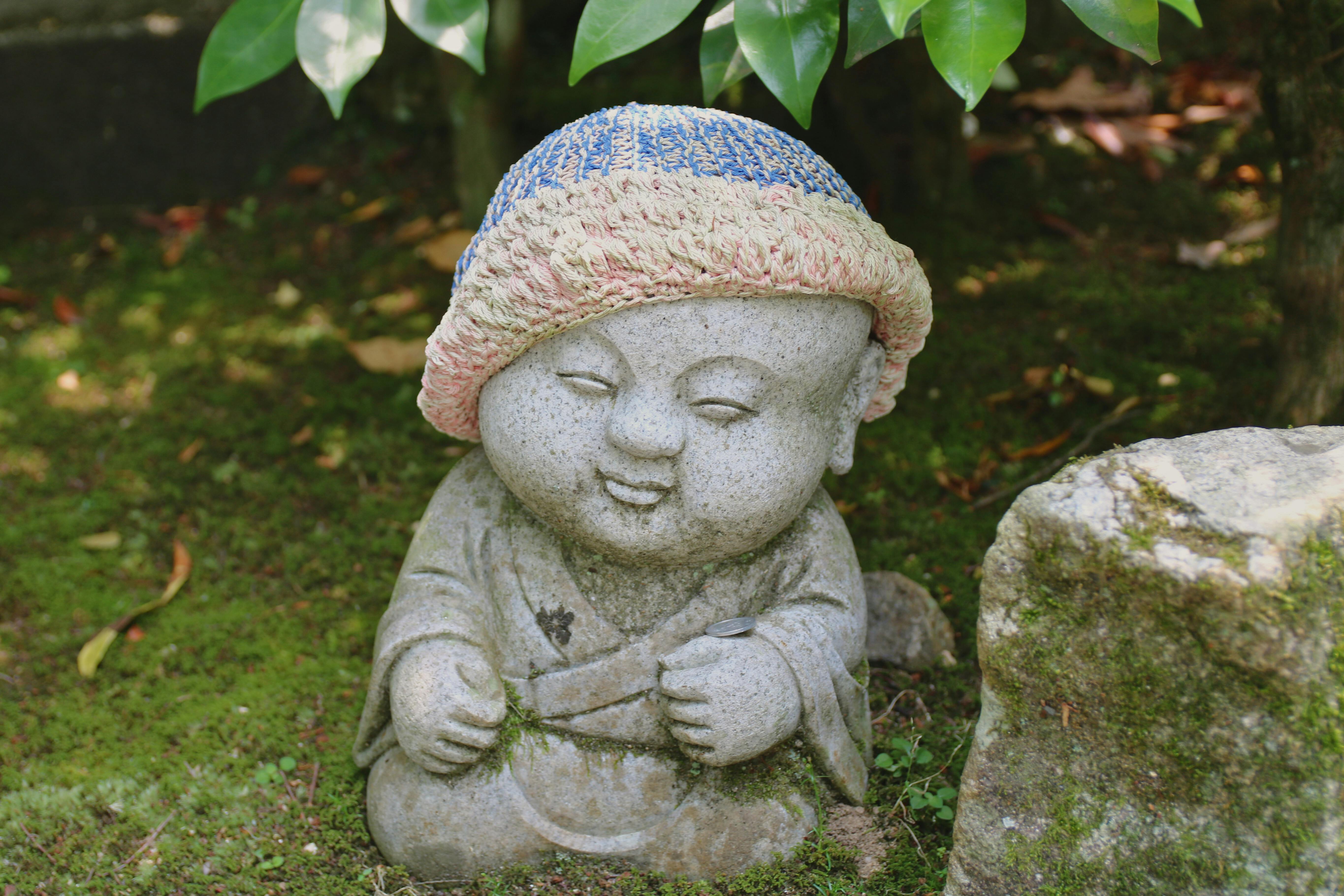 Little Buddha statue with a knitted cap in a serene Japanese garden. - Miyajima