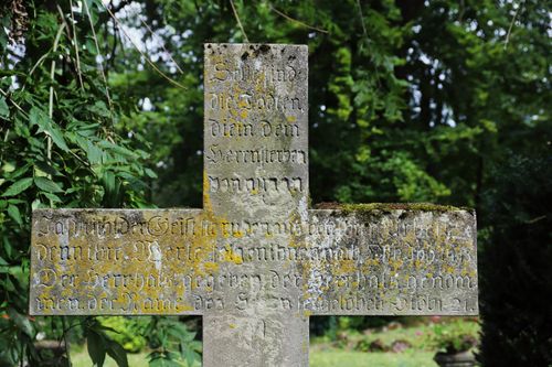 Free Weathered stone cross with engraved text in a German cemetery surrounded by greenery. Stock Photo