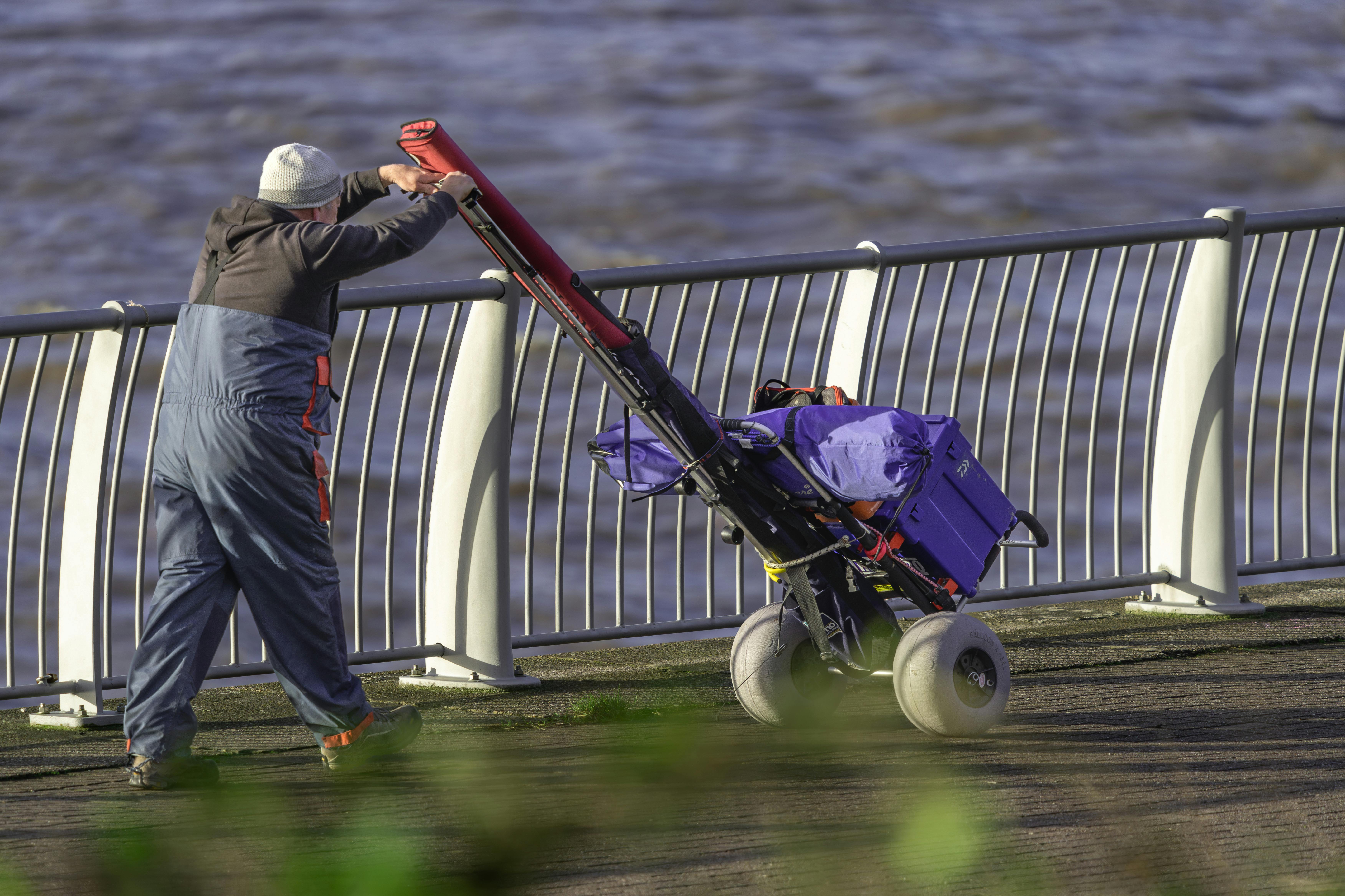 Man pushing cart along riverside railing · Free Stock Photo