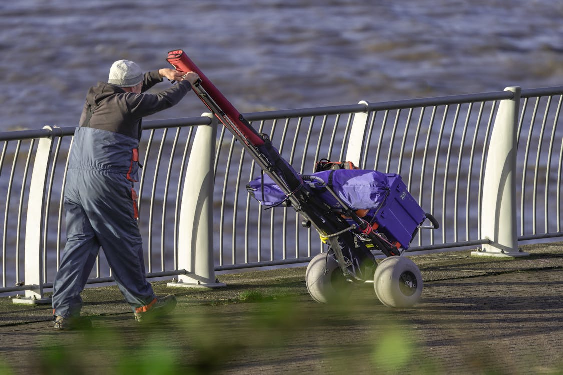 Man pushing cart along riverside railing · Free Stock Photo