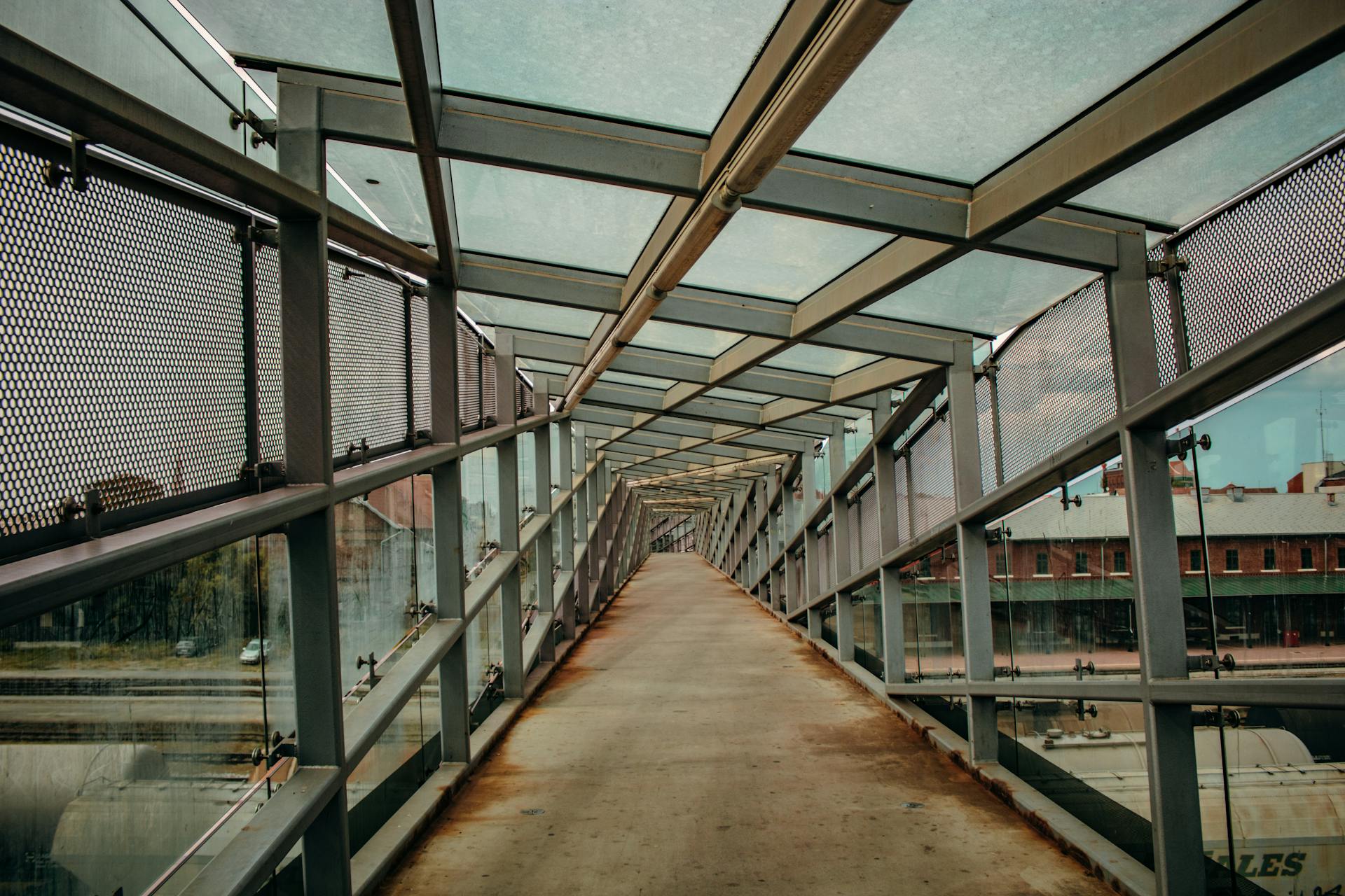 Long covered pedestrian bridge with glass roofing and metal structures, offering a clear view of the surroundings.