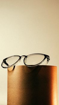 Minimalist image of eyeglasses on a gold cylinder with warm lighting, perfect for fashion or lifestyle showcases.
