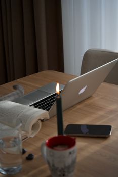 A serene workspace featuring a laptop, candle, mug, book, and smartphone on a wooden table.
