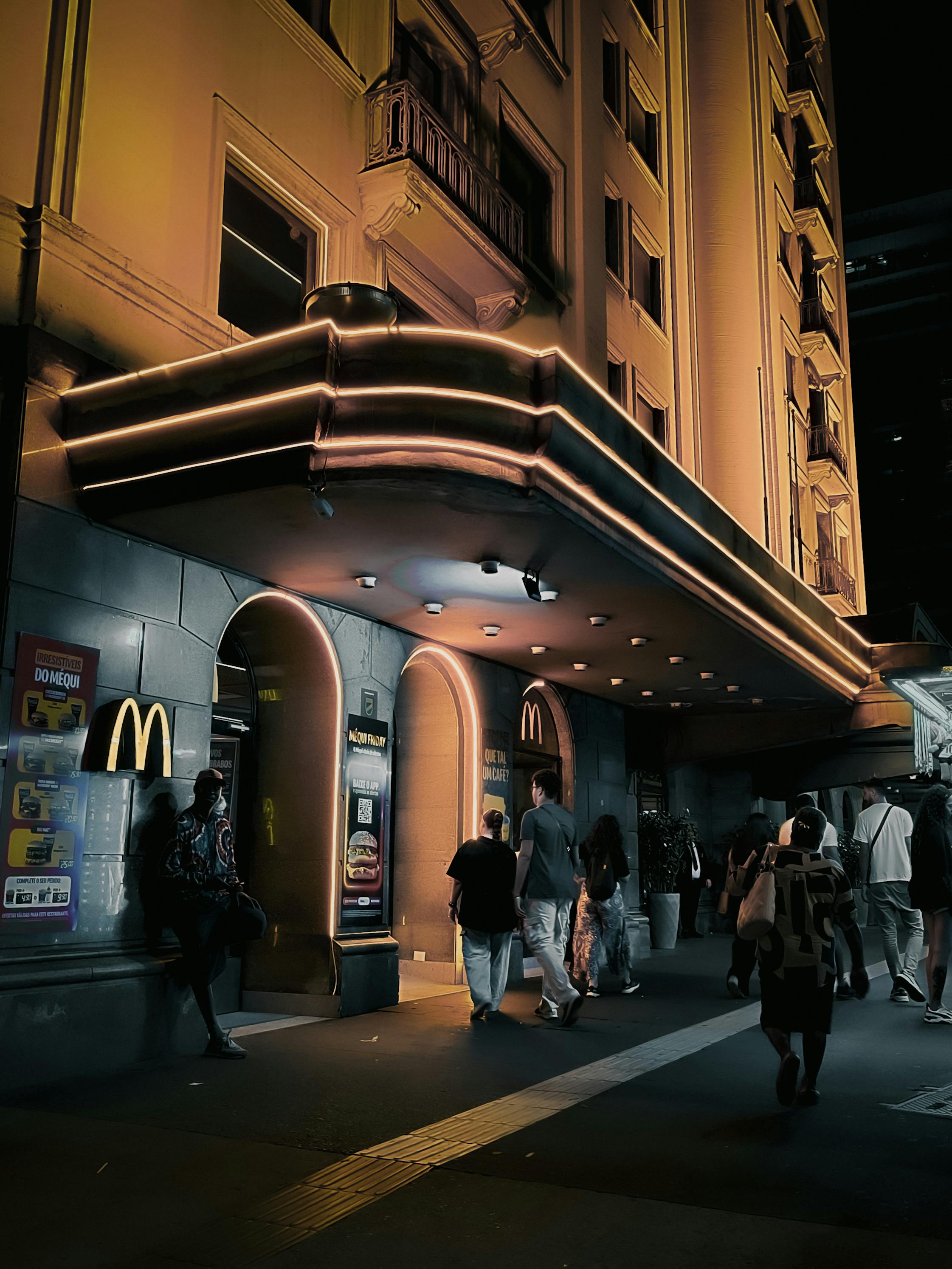 Ücretsiz Gece vakti, sıcak bir ışıkla aydınlatılmış retro tarzda bir binanın dışında insanların fotoğrafı. Stok Fotoğraflar