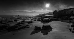 日落时分，黑白色调下，岩石海岸上一个人的剪影被拍摄下来