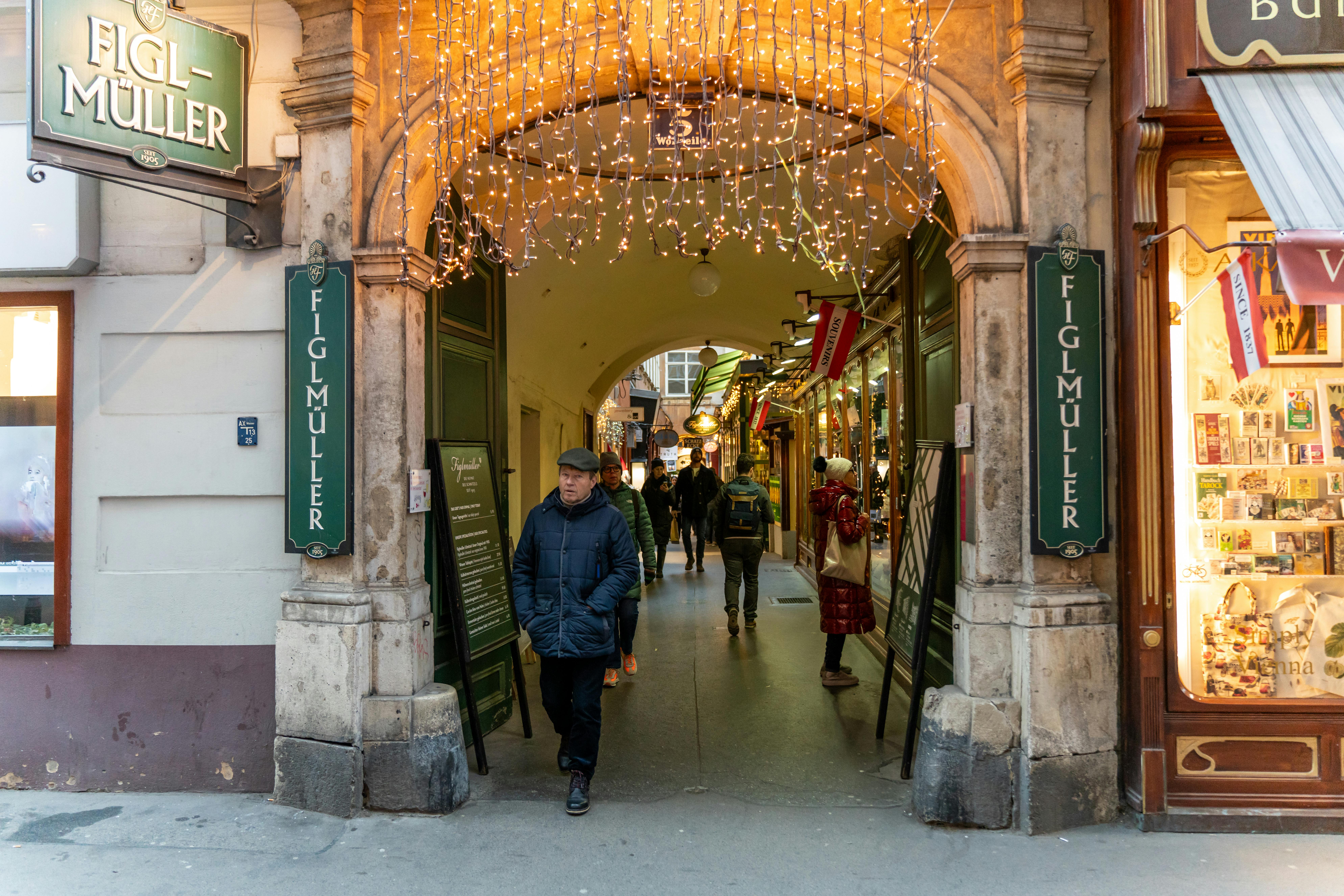 Historic Figlmüller restaurant entrance adorned with festive lights in Vienna's bustling street passage.