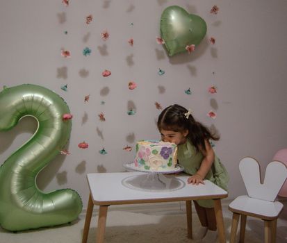 Young girl enjoys her second birthday with cake and balloons.