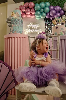 A happy toddler in a tutu celebrates a birthday with colorful decorations and balloons.