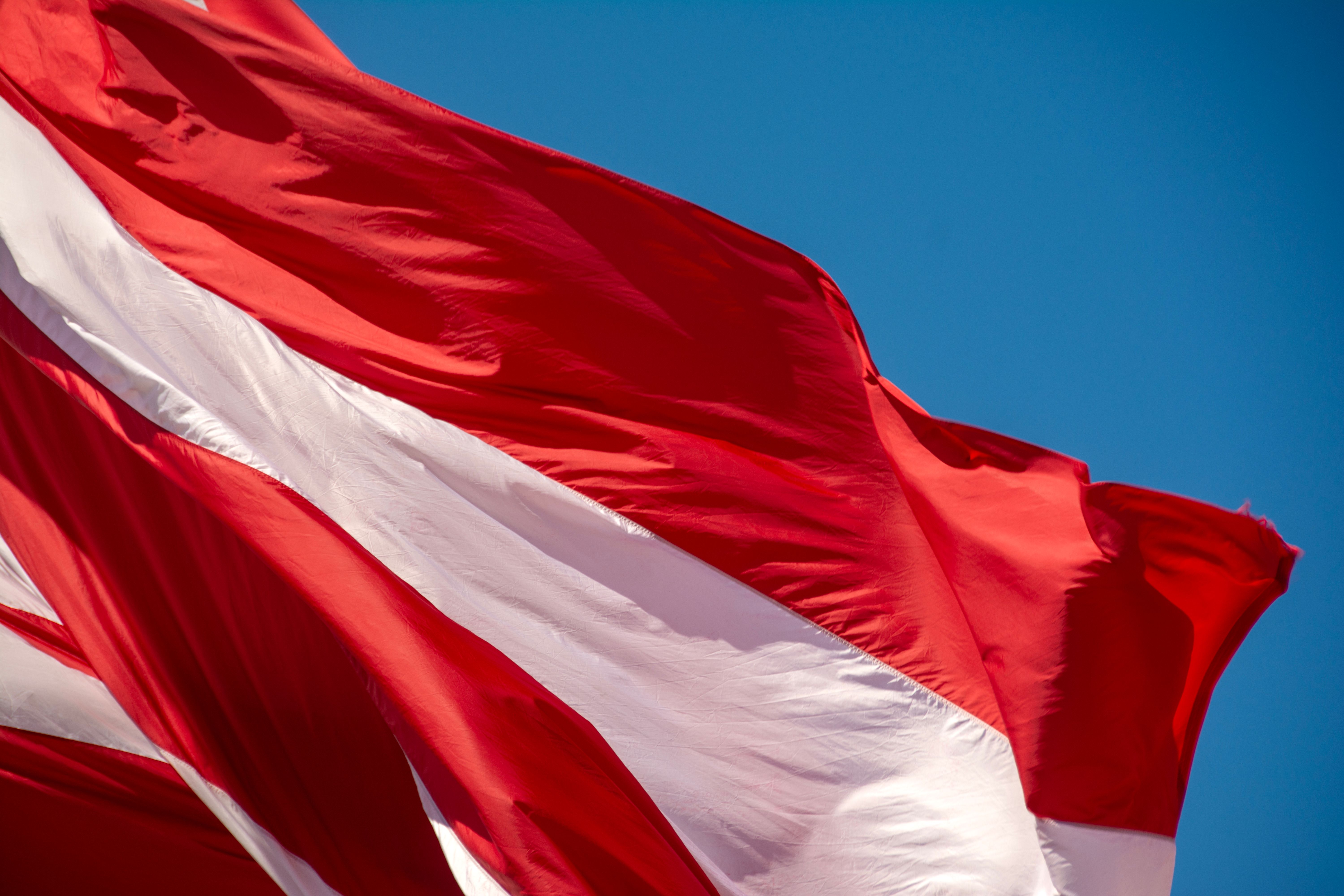 Vibrant Red and White Flag Against Blue Sky · Free Stock Photo