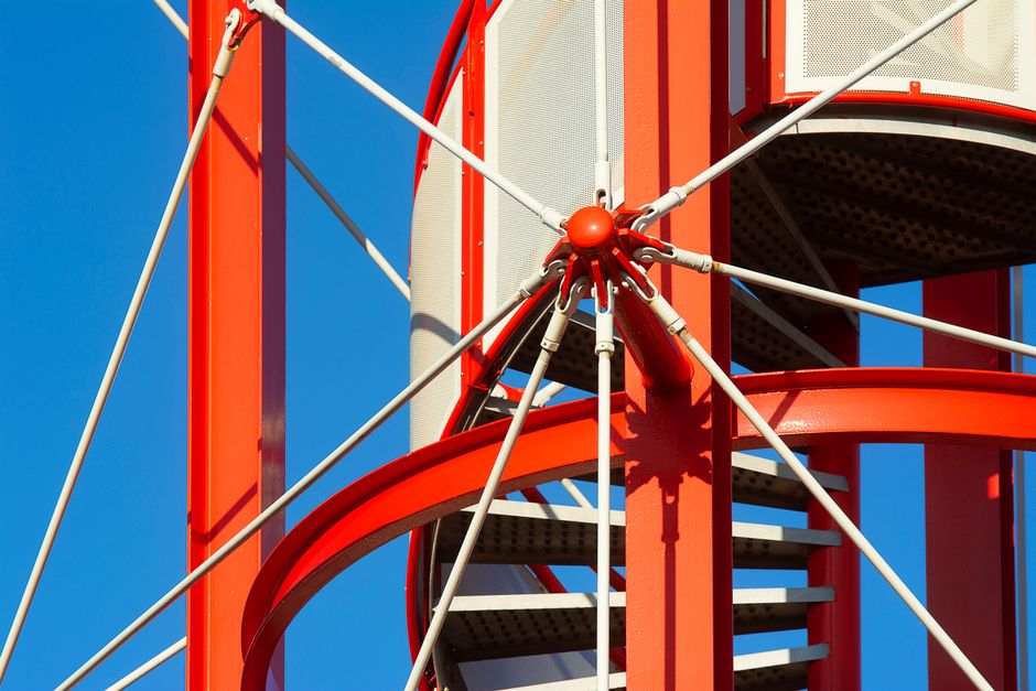 Dynamic red steel construction detail captured under clear blue sky, showcasing modern architecture.