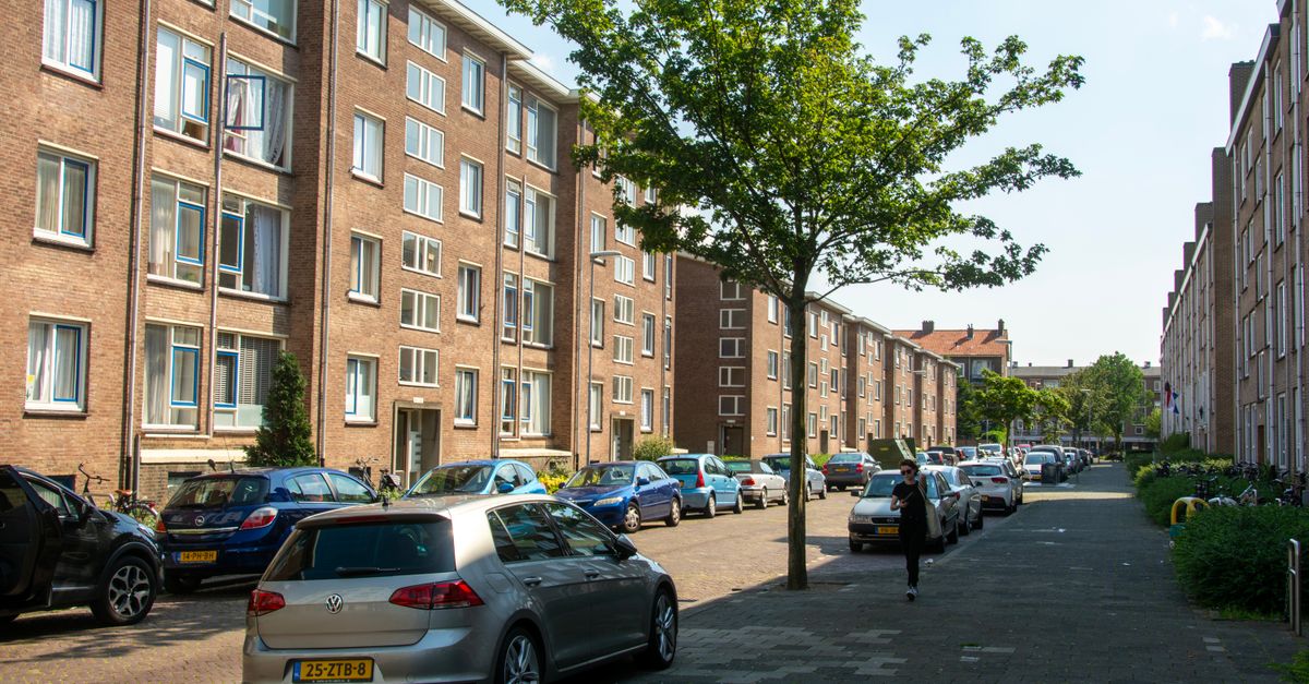 Urban street with parked cars and residential buildings on a sunny day.