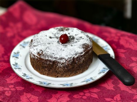 Decadent chocolate cake topped with a cherry, served on a floral plate - perfect for festivities.
