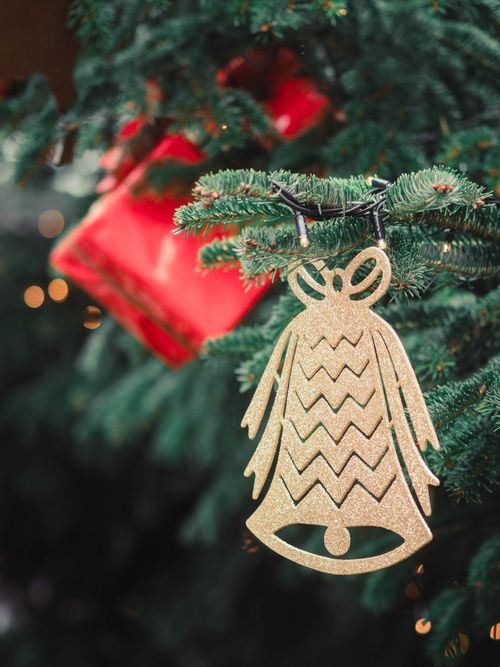 Free Close-up of a Christmas tree adorned with a gold bell ornament and red gift box. Stock Photo