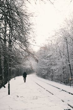 一个孤独的人穿过冬季森林，沿着白雪覆盖的铁轨