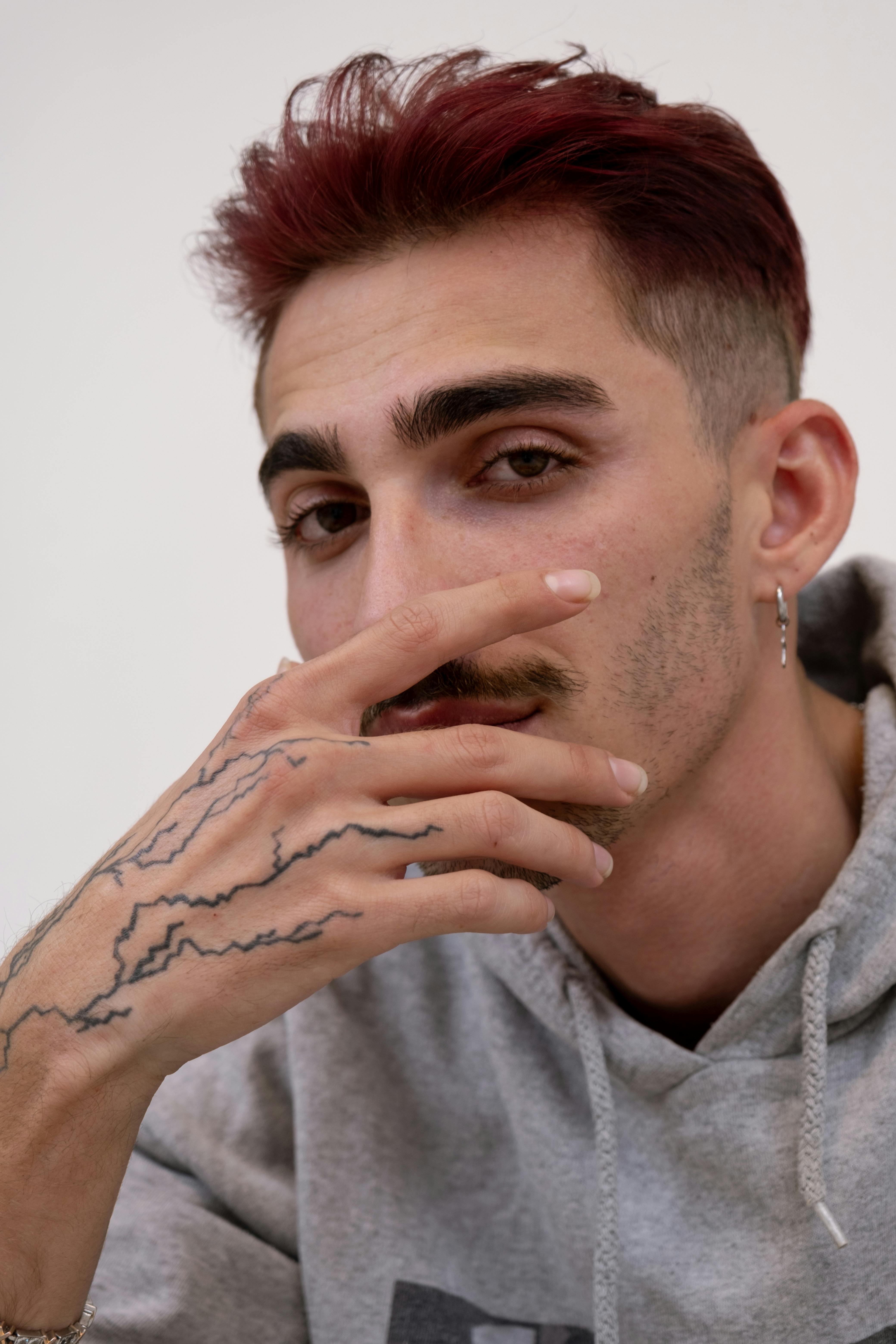 Close-up portrait of a young man with tattoos and red hair, exuding modern style.