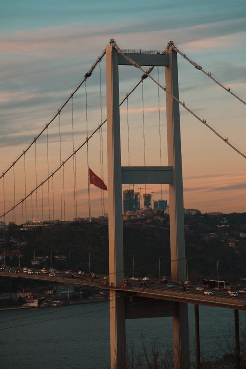 Free Breathtaking view of Bosphorus Bridge at sunset featuring the Turkish flag. A blend of architecture and natural beauty. Stock Photo