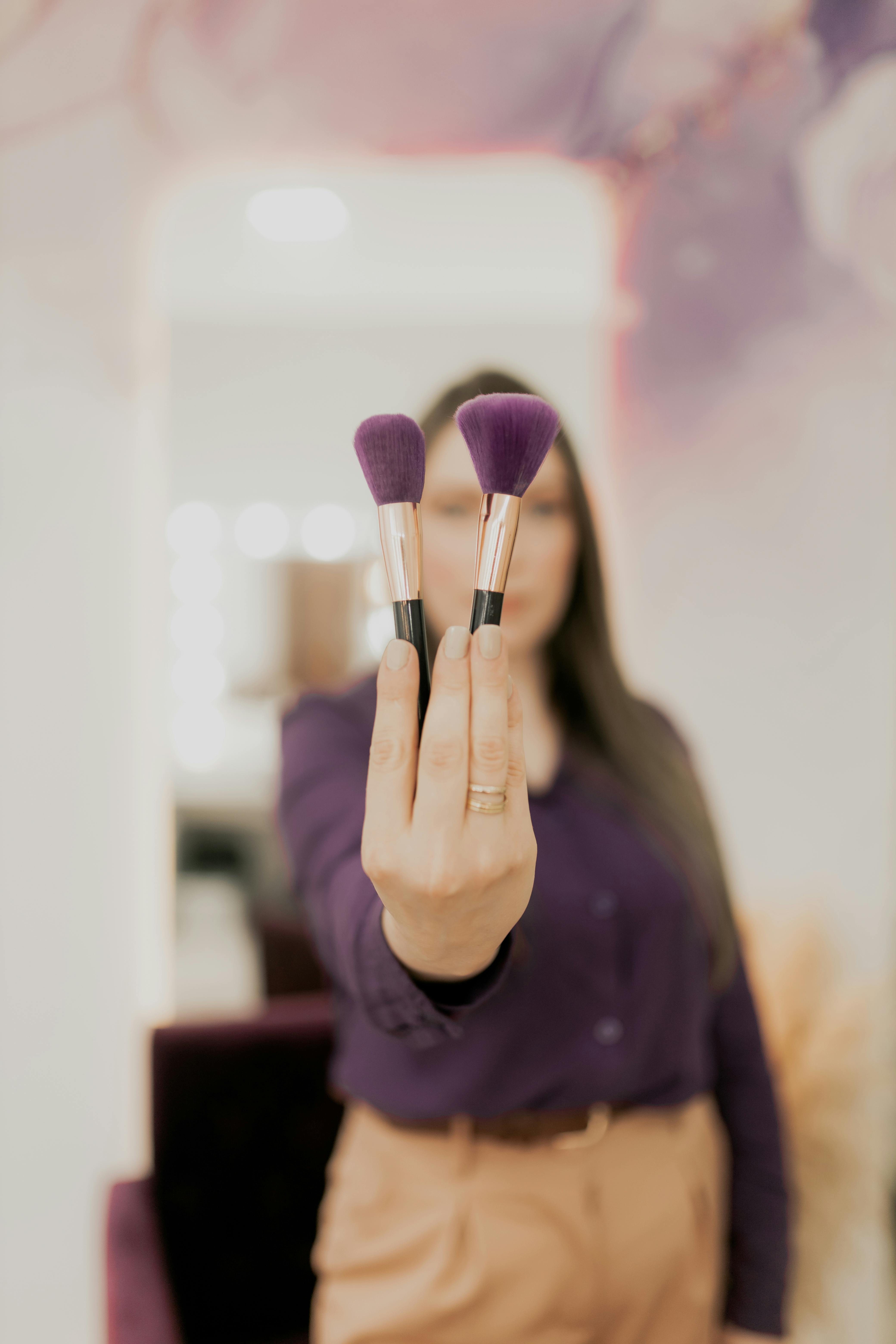 Miễn phí Một người phụ nữ cầm hai cây cọ trang điểm, tượng trưng cho vẻ đẹp và thời trang. Ảnh lưu trữ