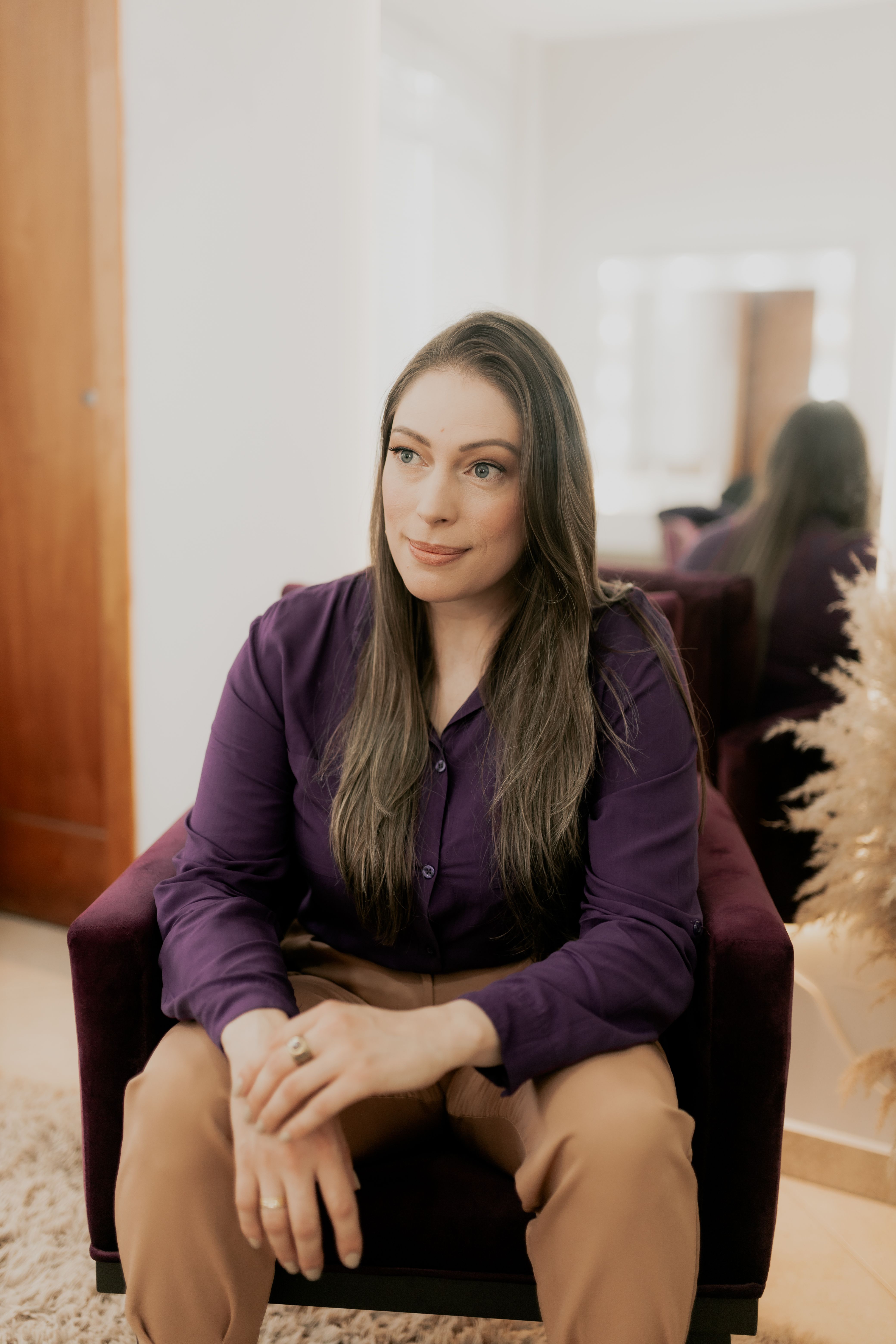 A woman in a purple shirt sits comfortably in a cozy indoor setting, conveying relaxation.