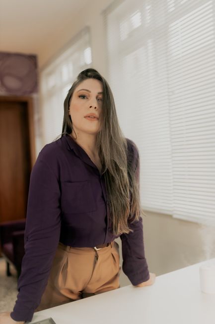Confident woman in a stylish purple blouse poses indoors, evoking elegance and poise.