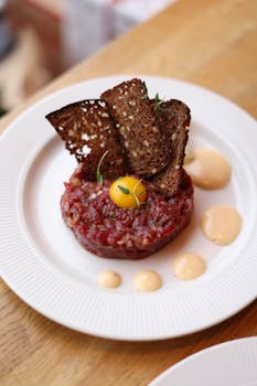 Delicious beef tartare with quail egg yolk, crispy toasts, and sauces on a white plate.