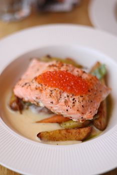 Grilled salmon served with vegetables and red caviar in a white dish.