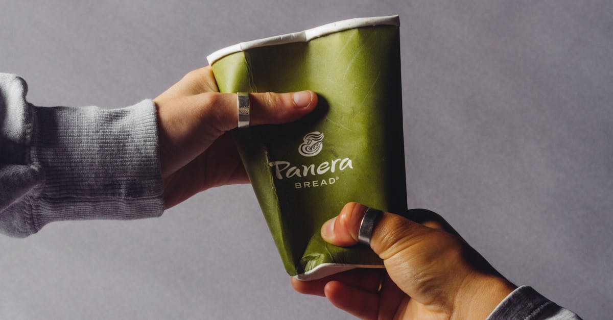 Close-up of two hands exchanging a crushed green disposable coffee cup indoors.