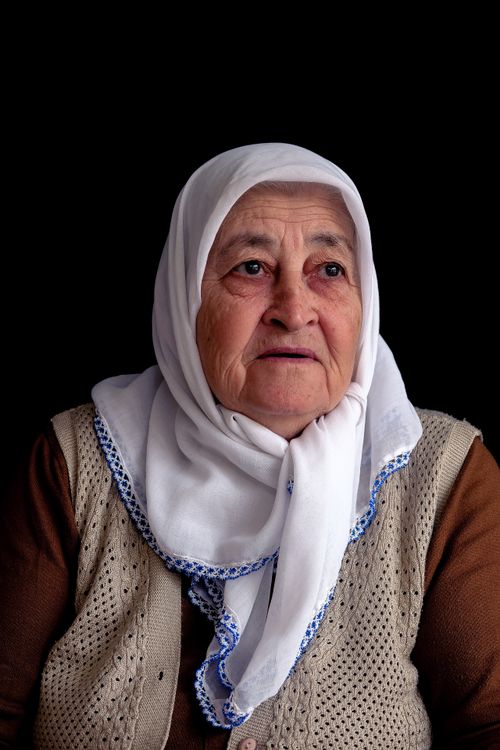 Free Portrait of an elderly woman wearing a white headscarf against a dark background. Stock Photo