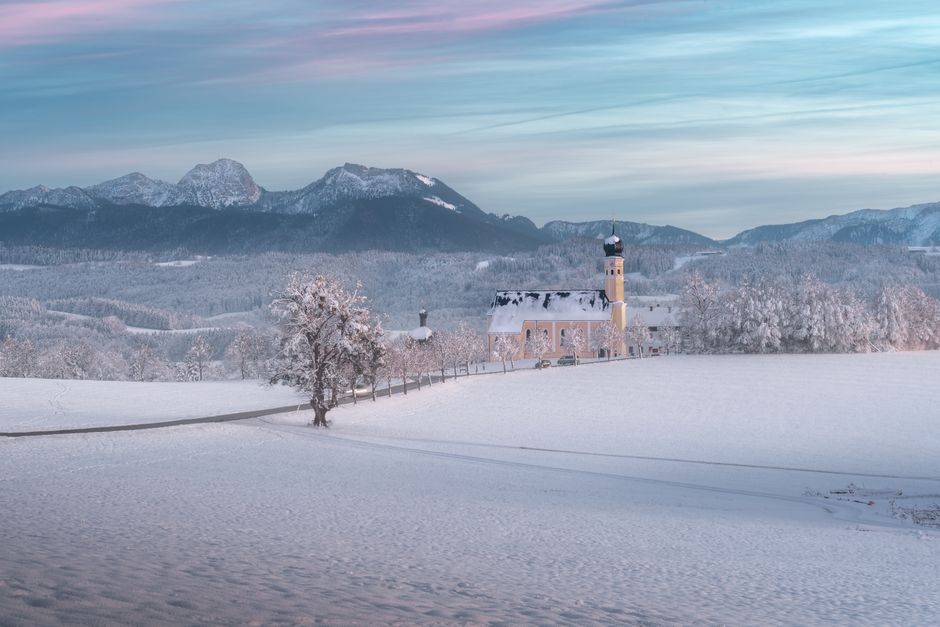 Idyllic winter scene of a snow-covered church with mountains in the background.