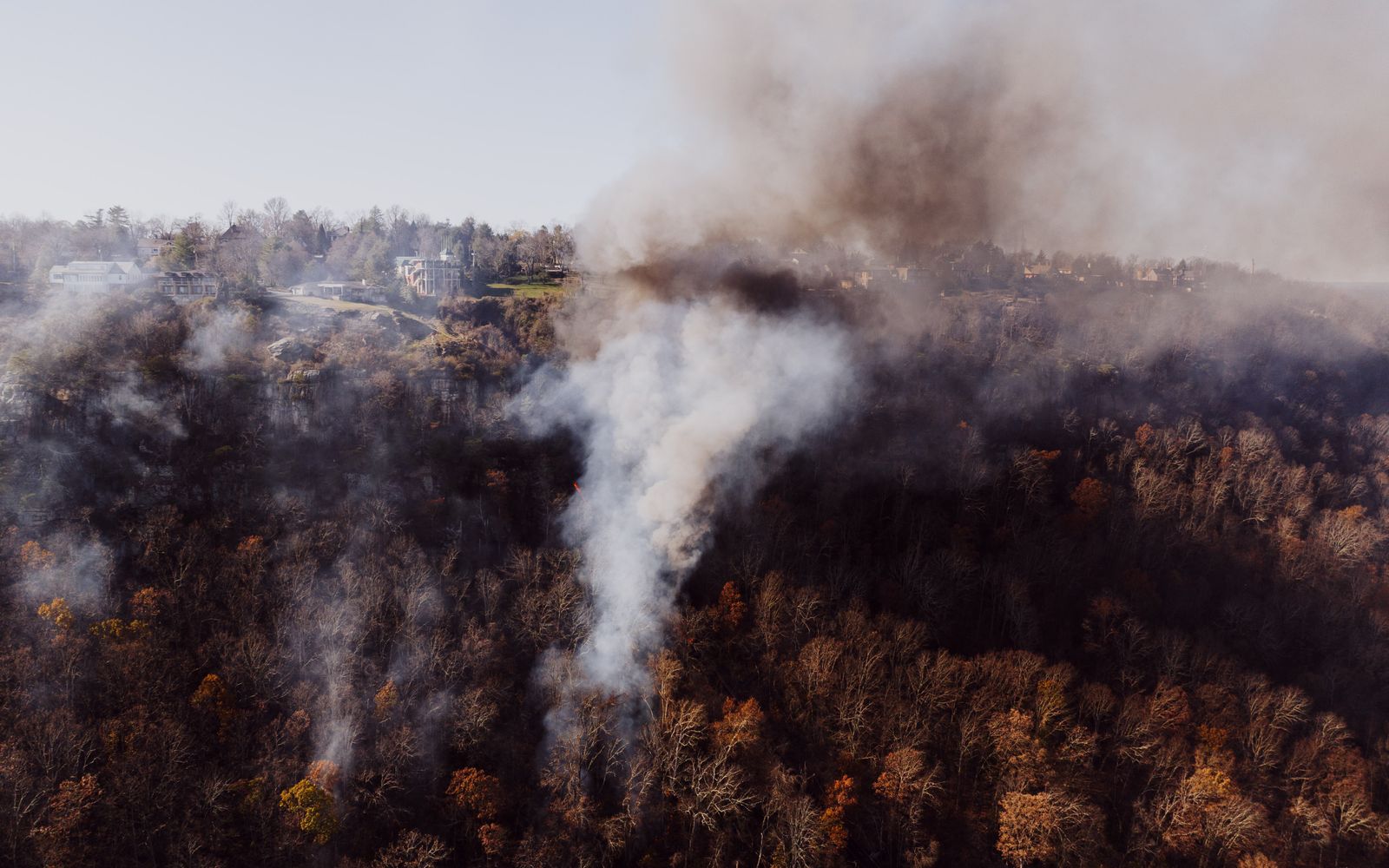 Aerial view of thick smoke rising from a forest fire over wooded hills