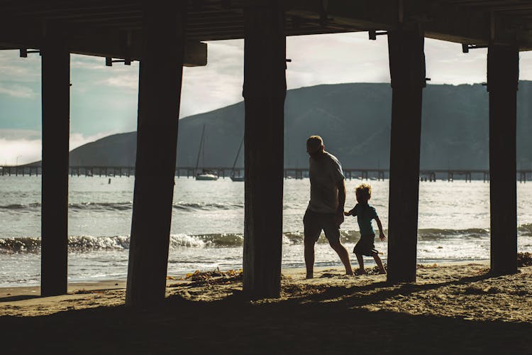 Man And Child Walking On Shore