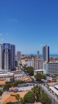 Aerial view of a modern city skyline with high-rise buildings and ocean backdrop, under clear blue skies.