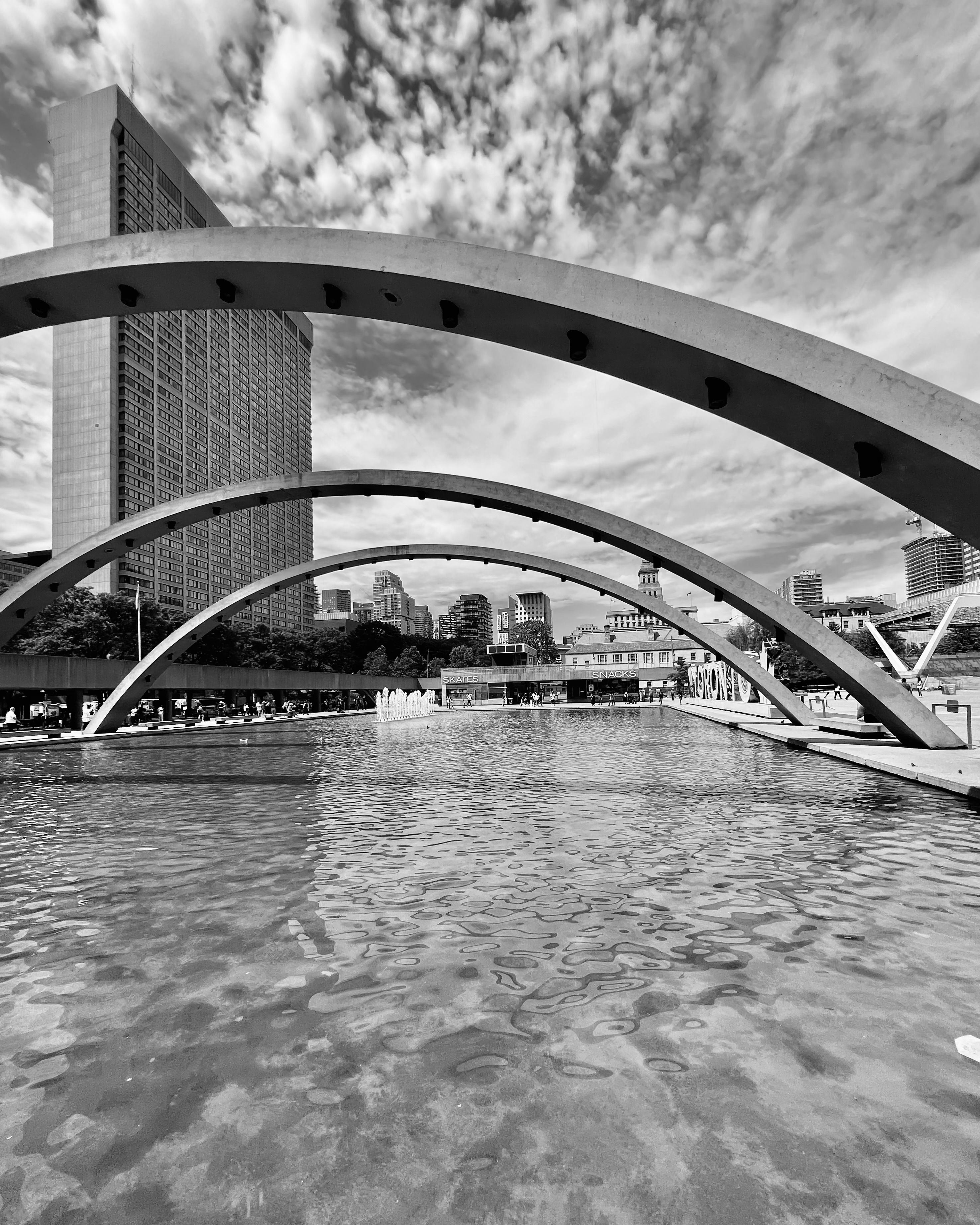 Black and white photo of city architecture featuring large arches over a reflecting pool.