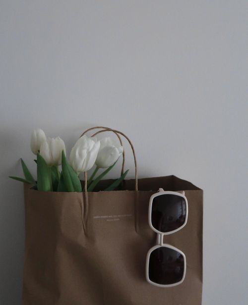Free Stylish minimalist image with a paper bag, white tulips, and square sunglasses against a white background. Stock Photo