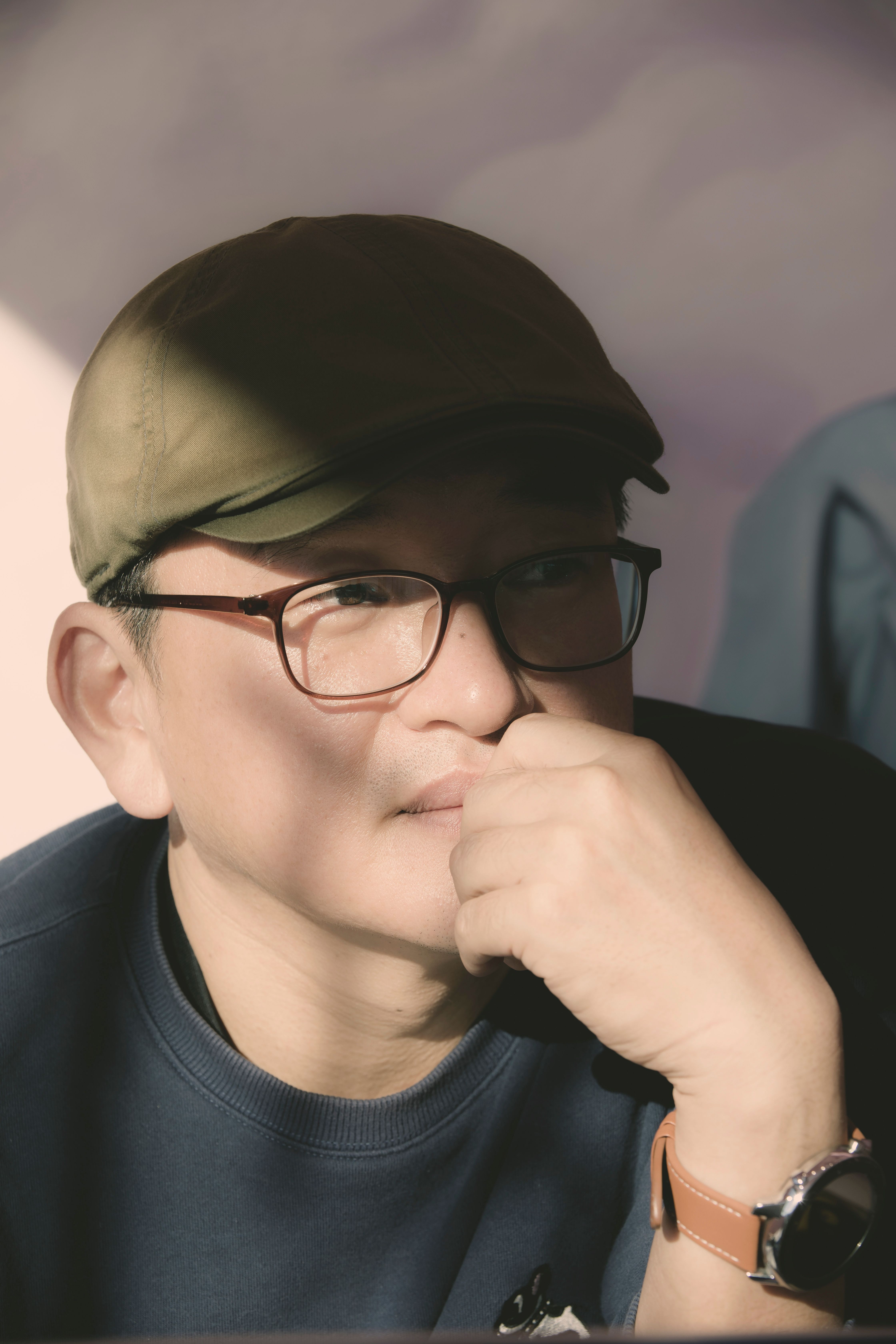 Man wearing a cap and glasses, deep in thought, with sunlight casting shadows.