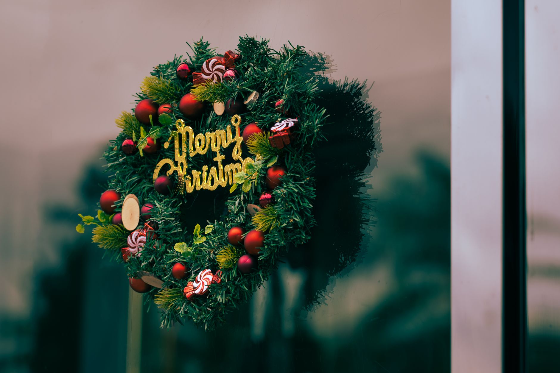Vibrant Christmas wreath with decorations and 'Merry Christmas' text on a glass door.