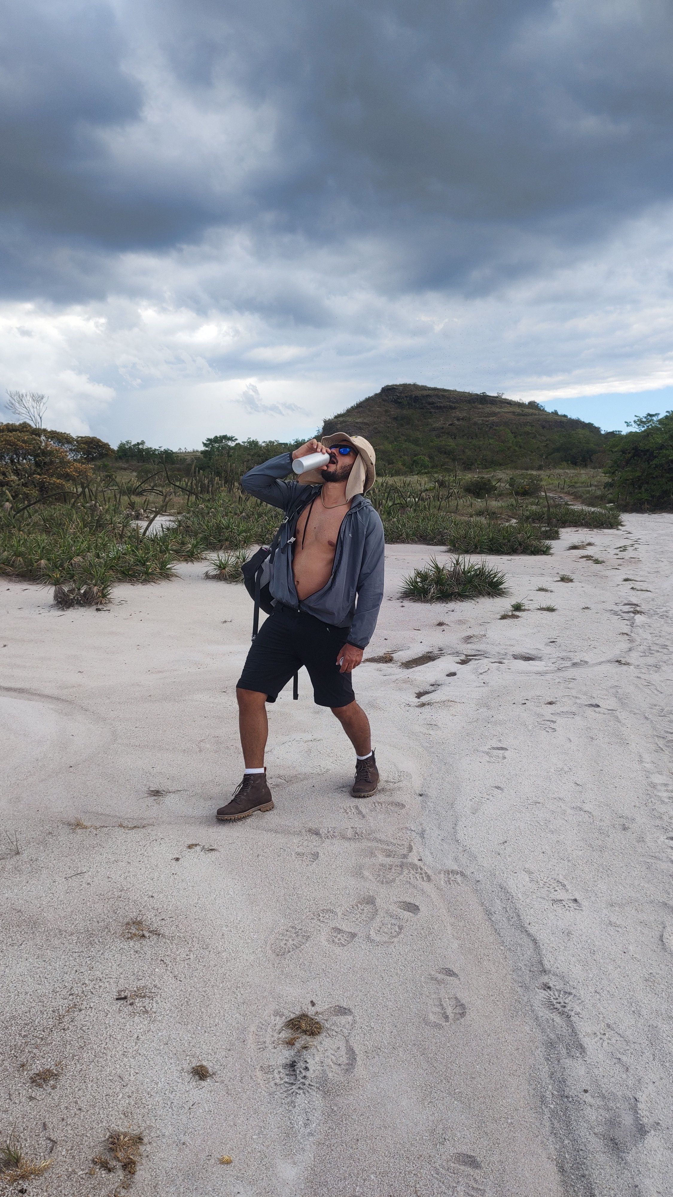 Man enjoys a cold beer in a scenic sandy desert under dramatic cloudy skies.