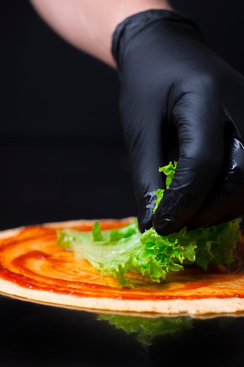 Person With Gloves Putting Lettuce on Pizza