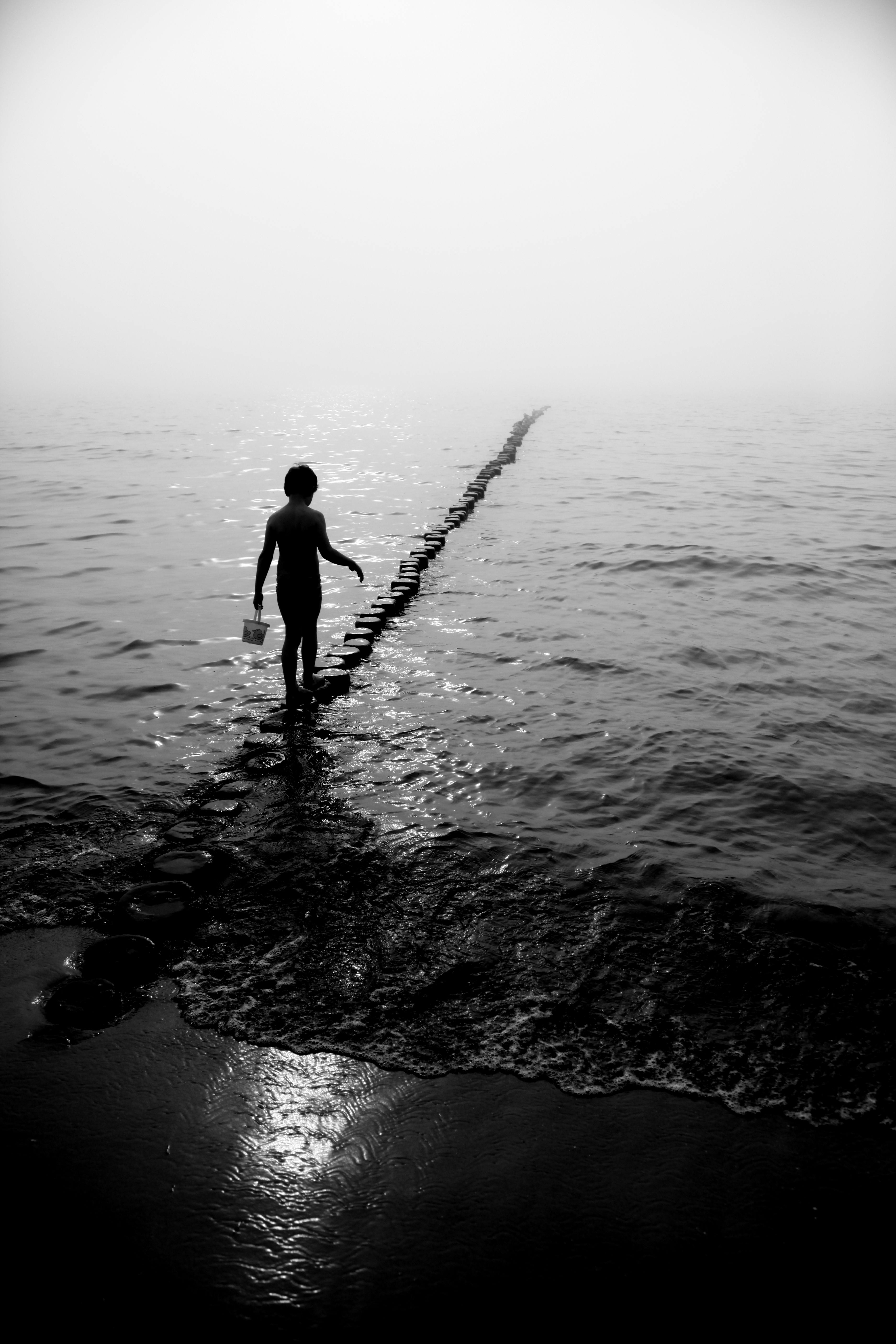 A mysterious black and white silhouette of a child walking into a foggy ocean scene.