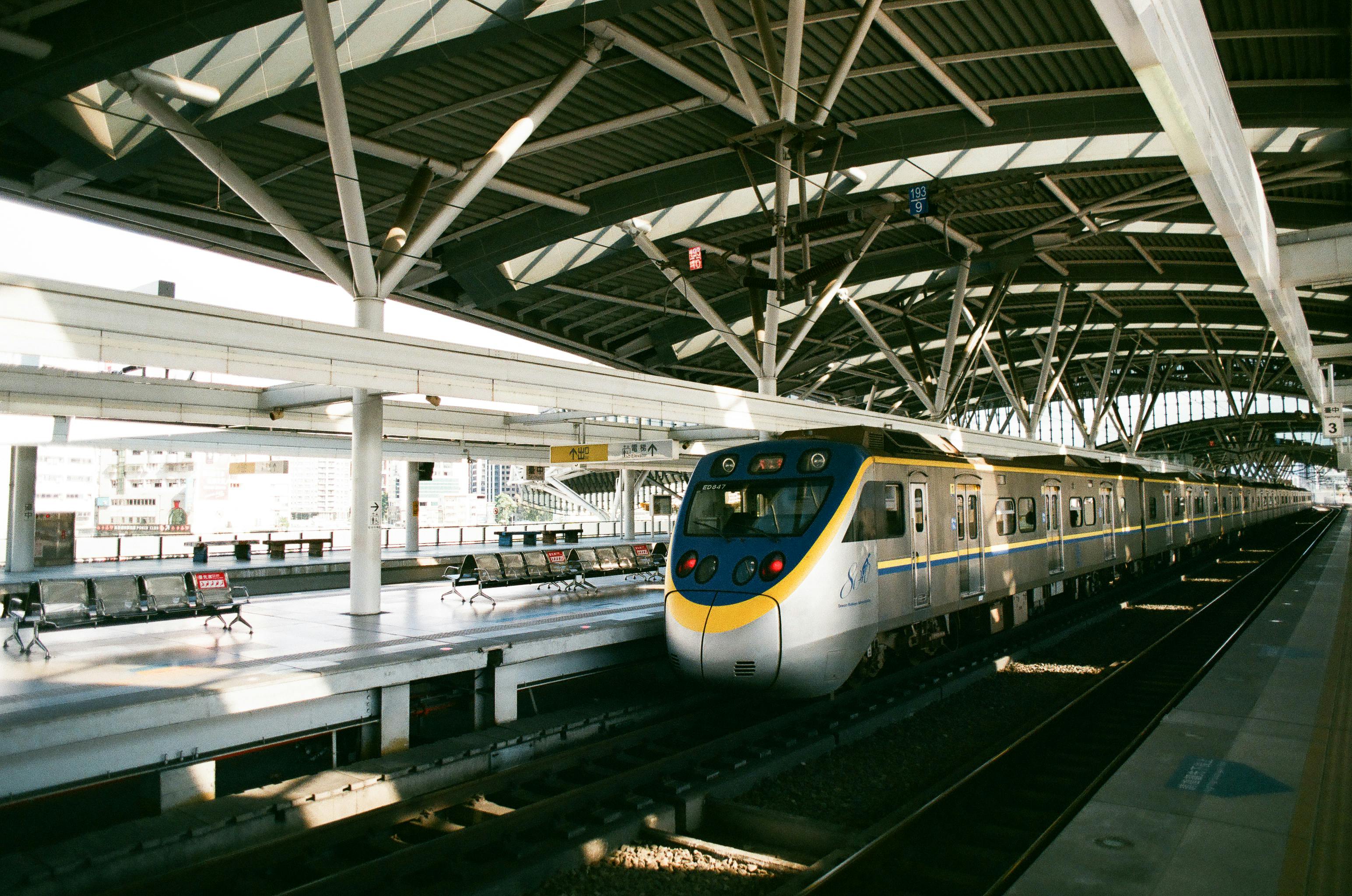 Commuter train awaits at a modern indoor station in Taiwan. Sunlight filters onto the platform.