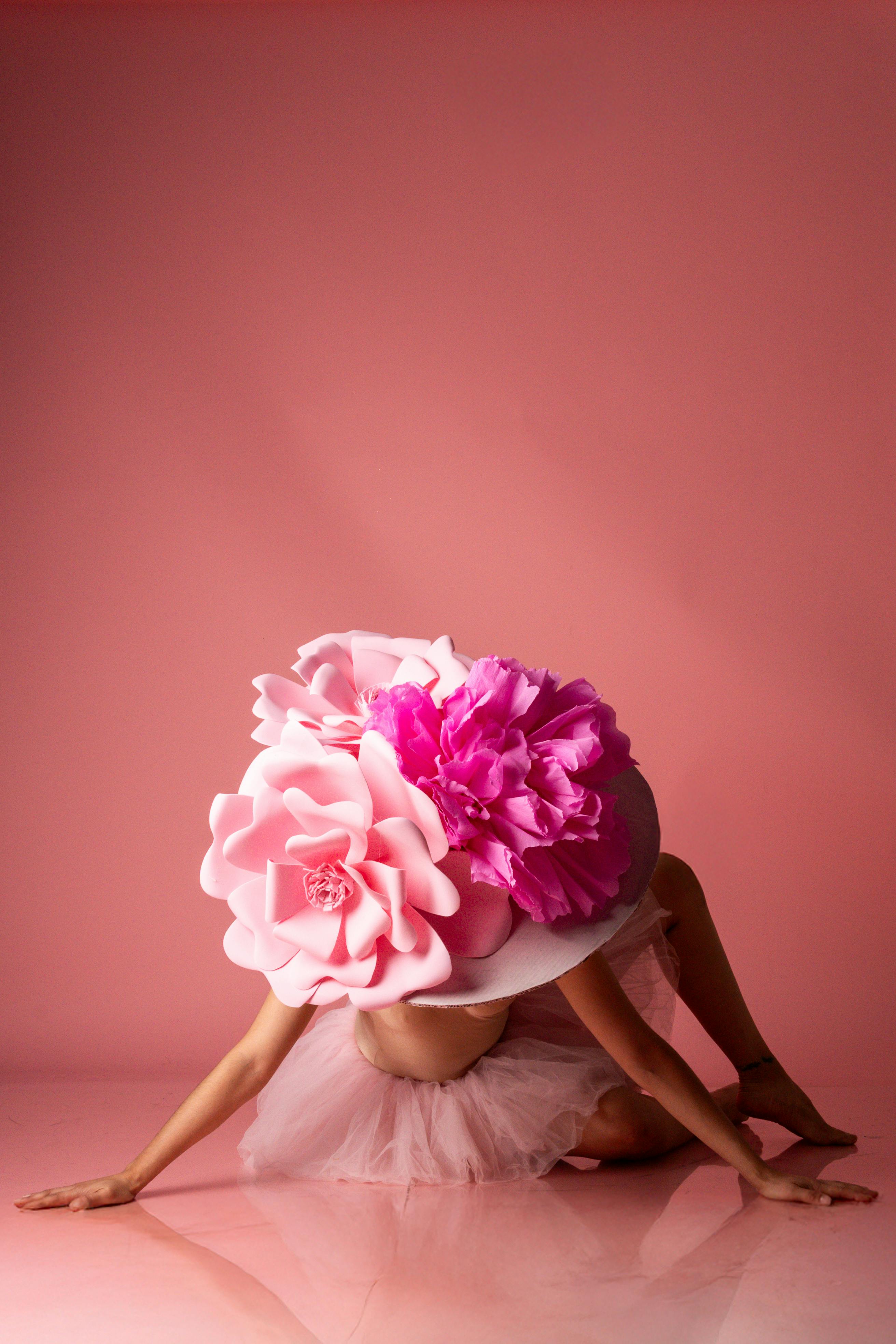 gratis Artistieke, hedendaagse danseres met een groot bloemenhoofddeksel in een roze setting, die een unieke expressie laat zien. Stockfoto