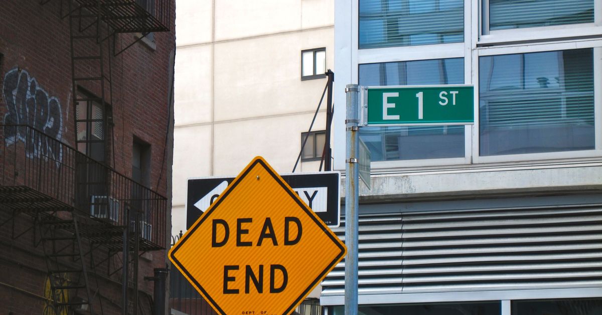 Dead end road sign at city intersection with signage and urban buildings.